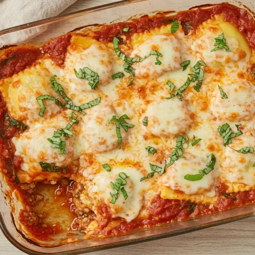 Close-up top-down view of the finished Baked Spinach Ravioli casserole in its 9x13 baking dish, showing bubbly sauce, golden melted cheese crust, garnished with fresh basil/parsley, looking natural and home-baked.